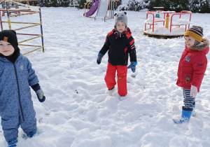 Dzieci stoją na śniegu w ogodzie przedszkolnym